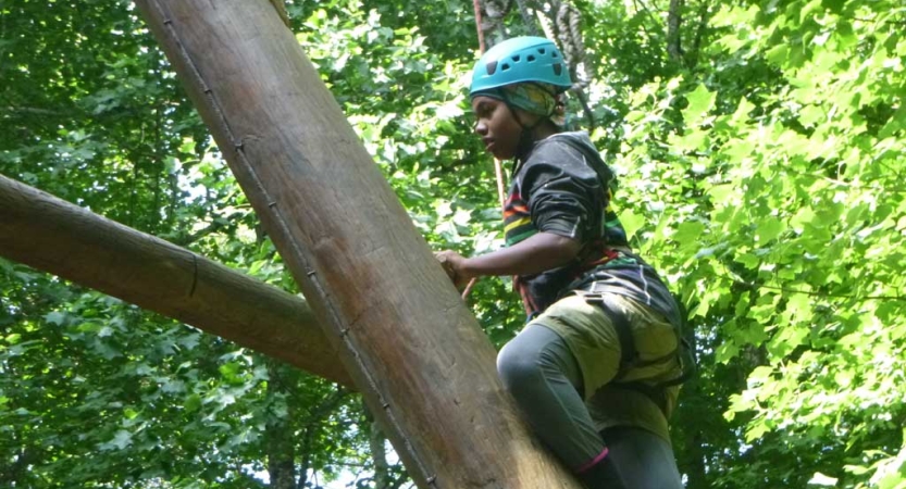 A person wearing safety gear is secured by ropes as they navigate a high ropes course. 